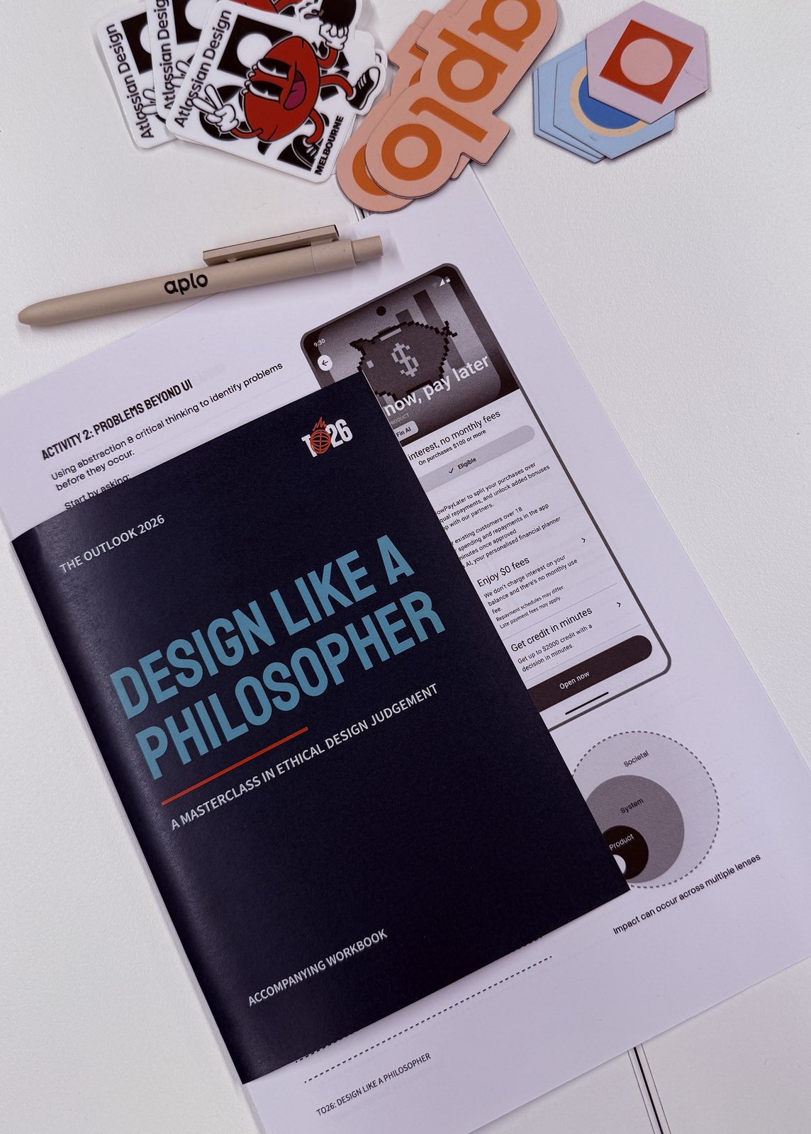 The Outlook 2026 Design Like a Philosopher accompanying workbook, laid out with event stickers and swag.